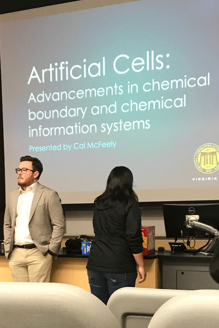 Clinton McFeely stands at the front of the classroom in front of a slideshow presentation projected on a screen