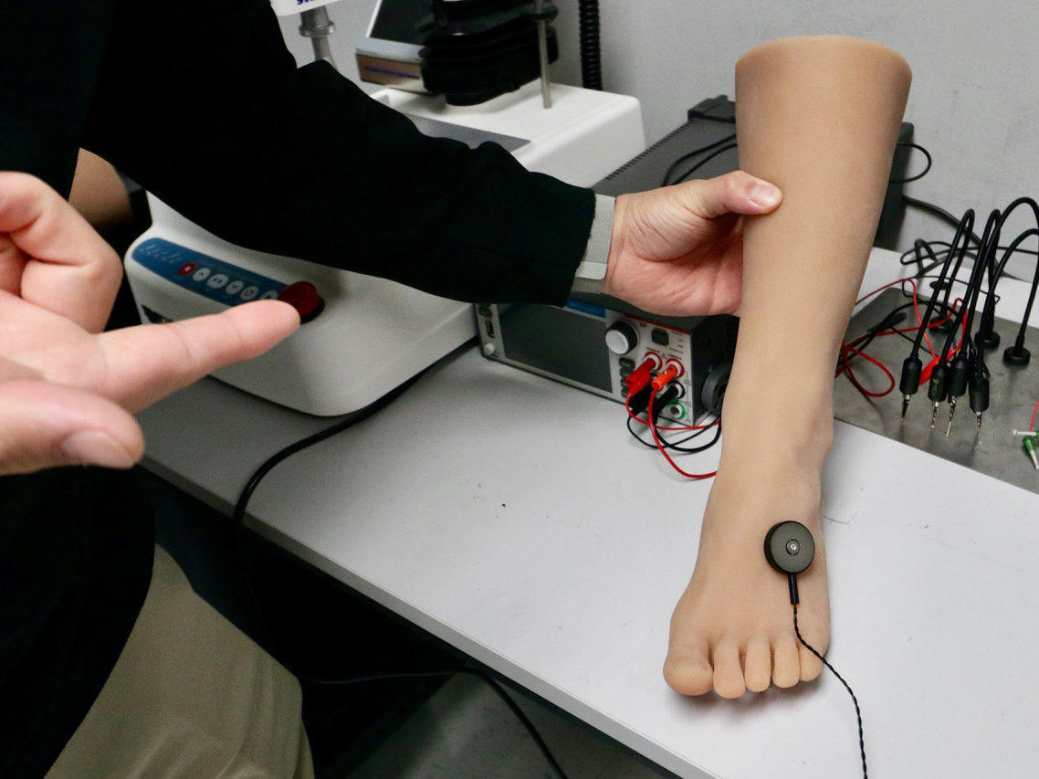 A lab worker holds a model lower leg with an electromagnetic actuator placed on top of the foot